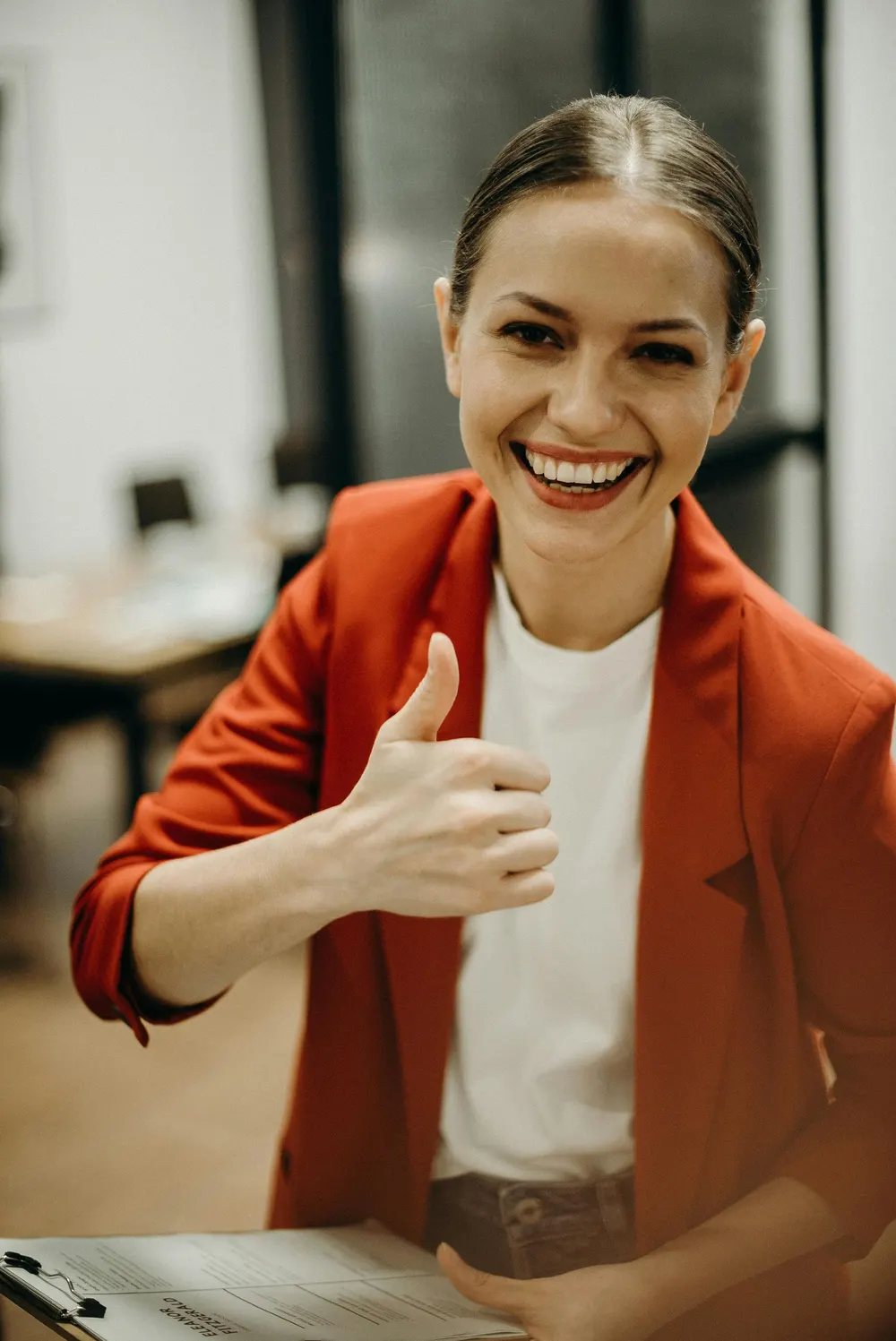 Smiling adviser in a red jacket giving a thumbs up from her desk